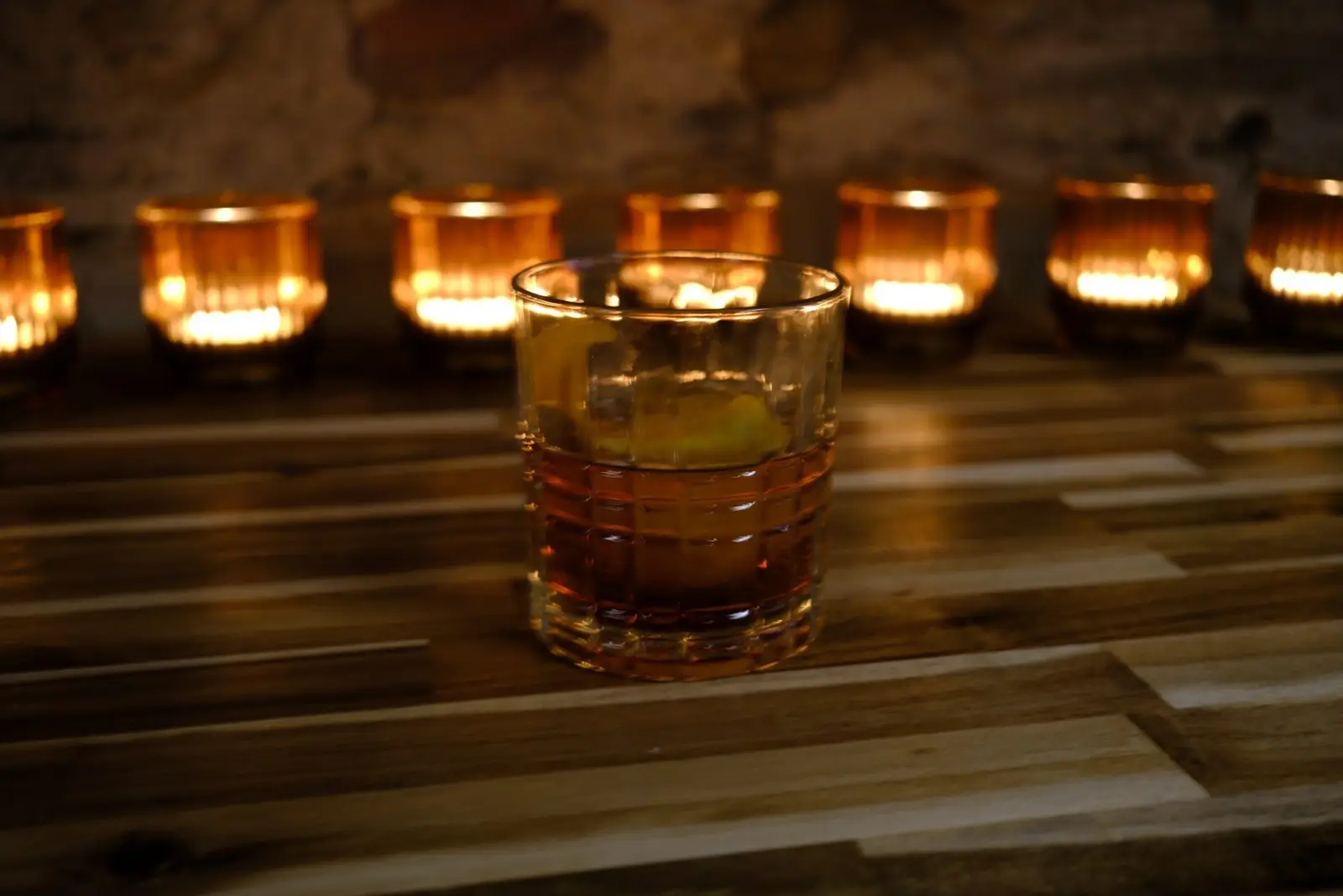 A bourbon on the rocks in front of a row of candles at Alpine Roots