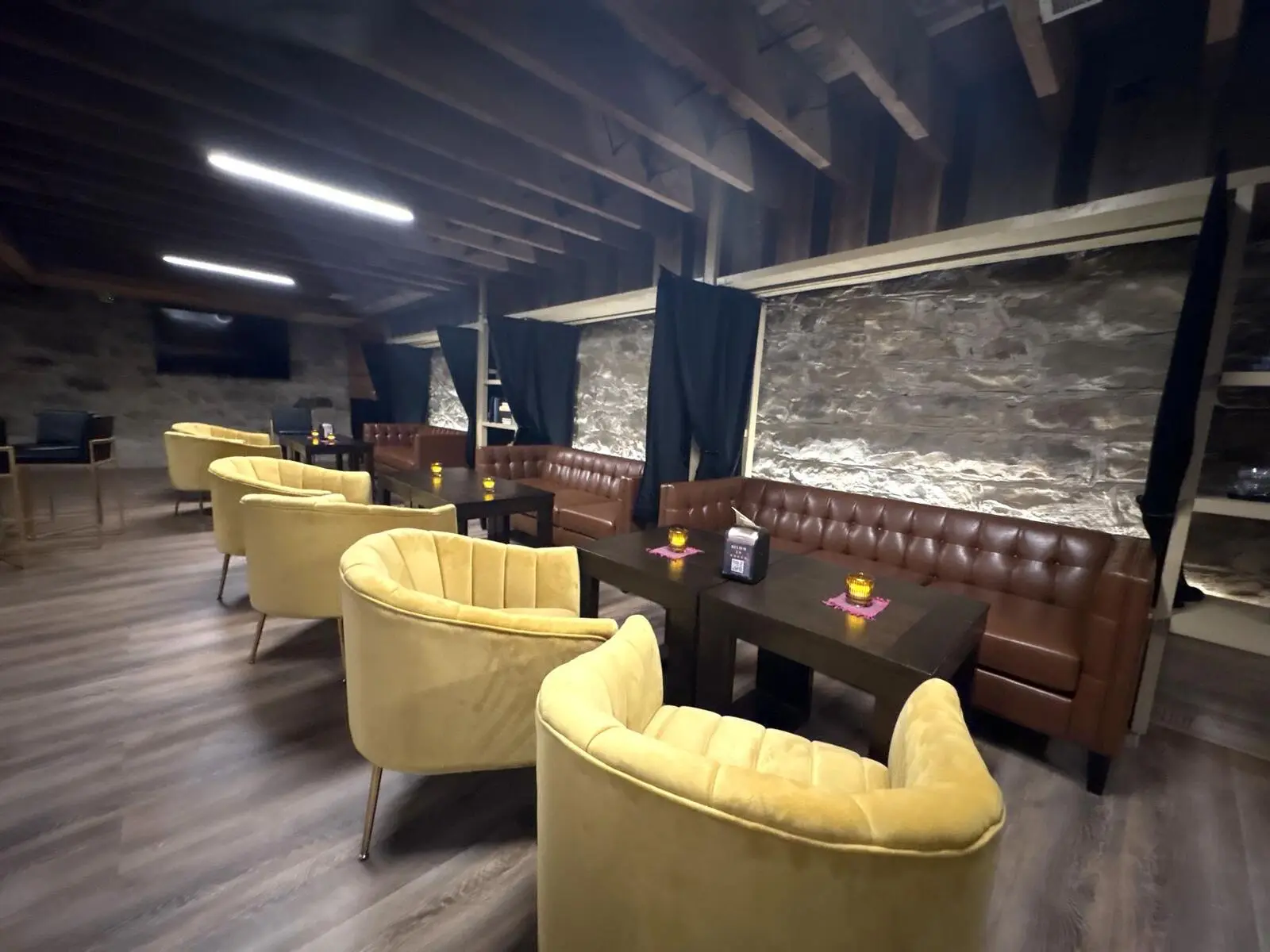 Alpine Roots downstairs: yellow velvet armchairs, a leather banquette and a stone wall lit by candles
