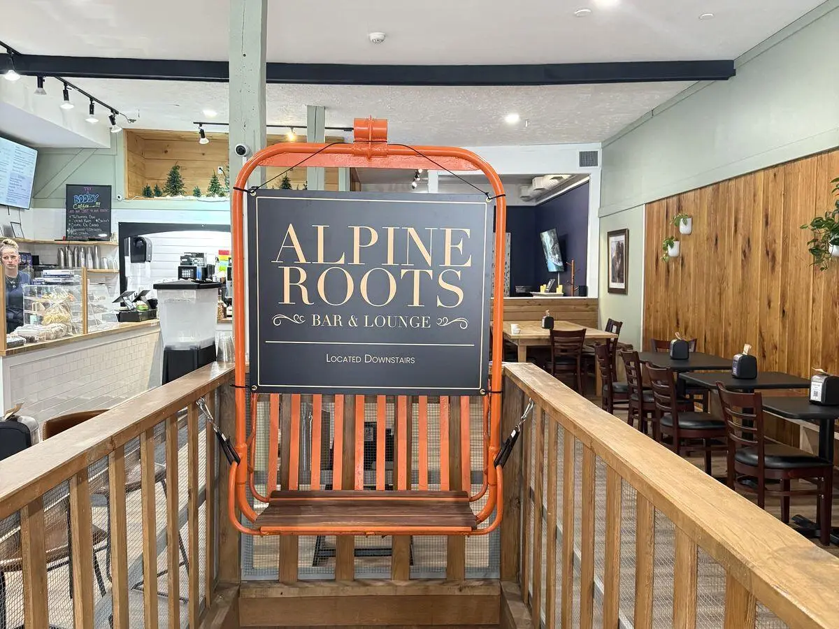 An orange chairlift seat carrying the Alpine Roots Bar & Lounge sign over the stairs down