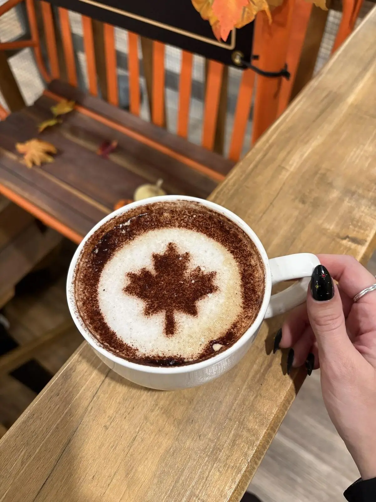 A latte with a maple leaf dusted on top, held over the orange chairlift bench