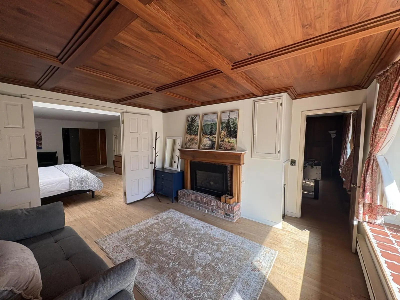 A sunny sitting room in the rental with a wood-beamed ceiling, a fireplace and a bedroom through the door