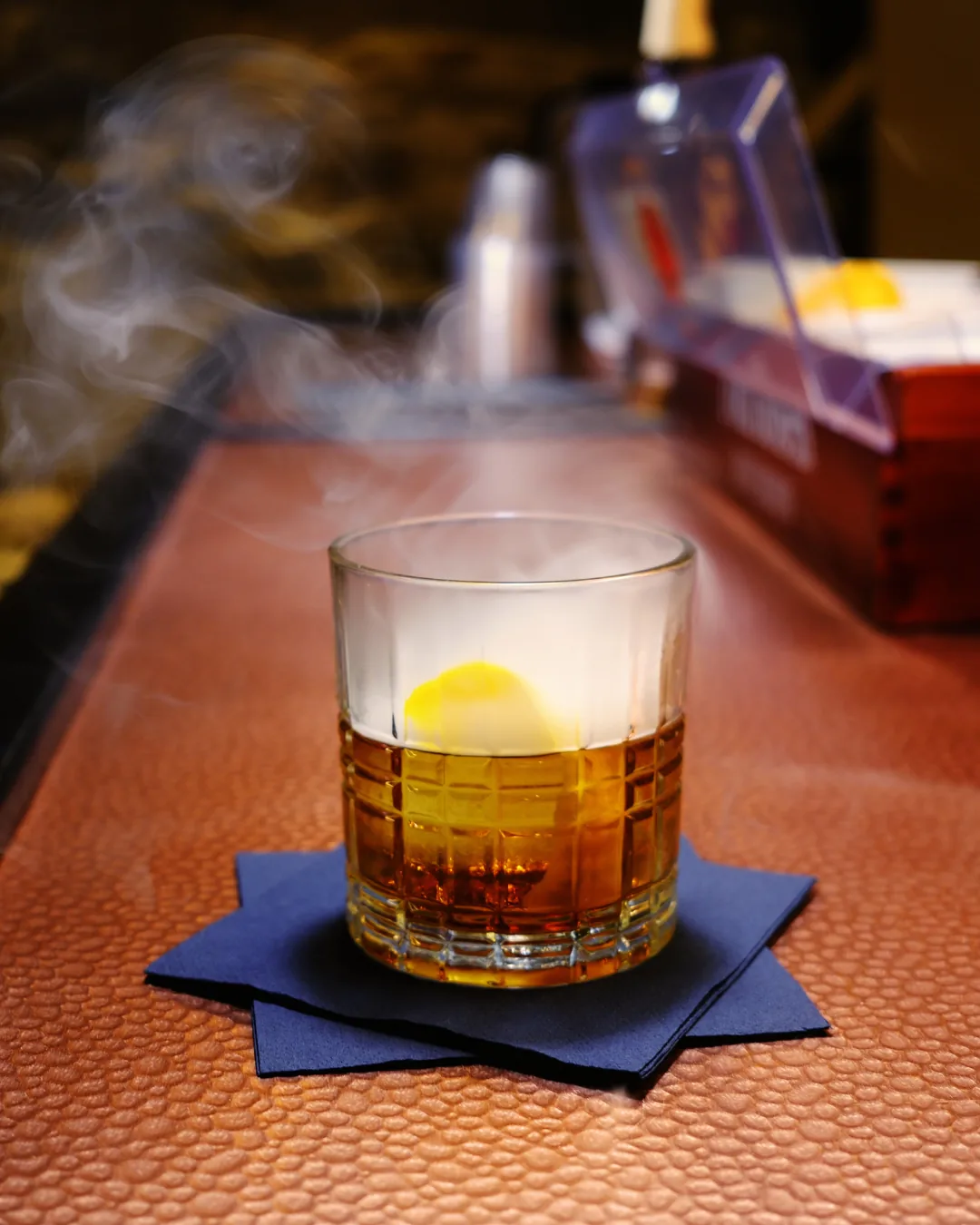 Cocktail with a lemon twist served over ice, smoke rising from the glass