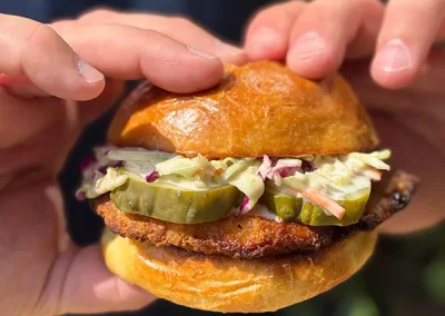 Hands holding a fried chicken sandwich with pickles and slaw on a brioche bun